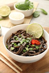 Tasty buckwheat noodles (soba) with sauce, onion and lime in bowl on table
