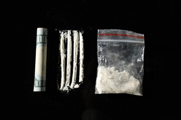 Drug addiction. Plastic bag with cocaine and rolled dollar banknote on black background, flat lay