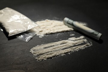 Drug addiction. Plastic bag with cocaine and rolled dollar banknote on grey textured table, closeup