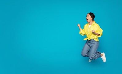 Excited young woman in mid-air jump with a fist pump, wearing a bright yellow blouse