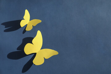 Yellow paper butterflies on dark blue background, top view. Space for text