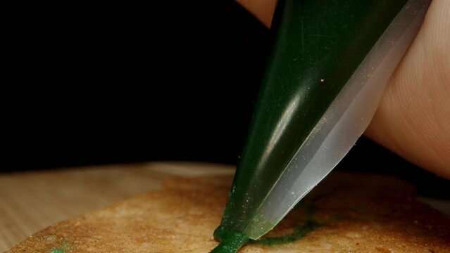 The pastry chef applies green icing from the bag to decorate gingerbread. Dolly slider, close up.