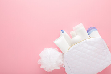 White cosmetic travel bag with plastic bottles and bathing sponge on pink table background. Care...