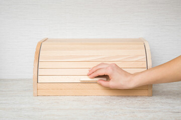 Young adult woman hand opening or closing wooden bread box on table top at home kitchen. Closeup. Front view. - obrazy, fototapety, plakaty