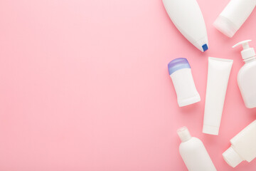 Different white plastic cosmetic bottles on light pink table background. Pastel color. Care about clean and soft body skin. Daily beauty products. Closeup. Empty place for text. Top down view.