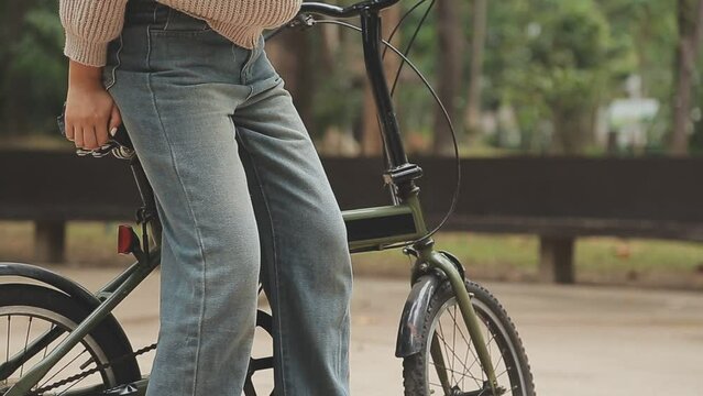 Young pensive dreamful happy woman 20s wearing casual green jacket jeans riding bicycle bike on sidewalk in city spring park outdoors, look aside. People active urban healthy lifestyle cycling concept