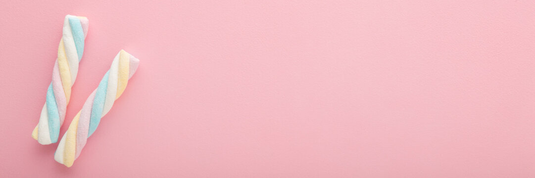Two colorful swirl soft marshmallow candies on light pink table background. Pastel color. Sweet snack closeup. Wide banner. Empty place for text. Top down view.