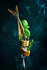 Smoked mackerel fish on a metal fork. Pieces of juicy smoked fish. On a black background. - obrazy, fototapety, plakaty