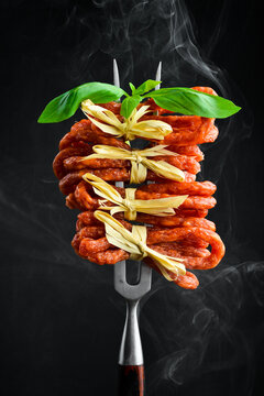Smoked kabanos sausages with herbs. on a metal fork. On a black background, vertical photo.