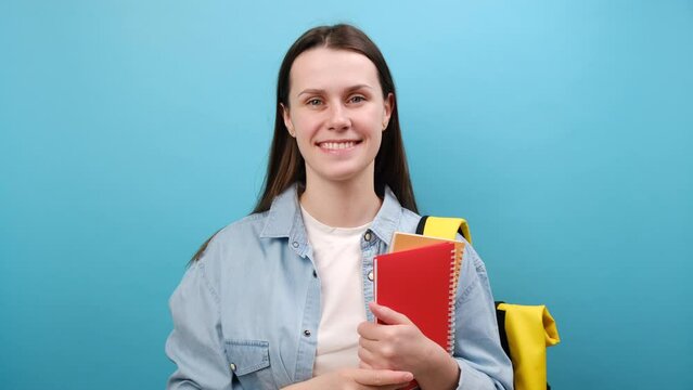 Portrait of young woman student in shirt with backpack pointing on camera, you come to me, come here, calling beckoning, coming closer, isolated on blue background. Education in high school concept