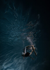 Underwater shoot of beautiful ballerina in white dress swimming and dancing in water through sunbeams.