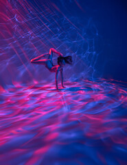 Underwater shoot of ballerina swimming and dancing in water through pink and red light rays.