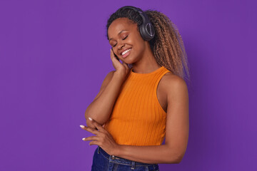 Young kind positive African American woman millennial wearing headphones feels tenderness and good...