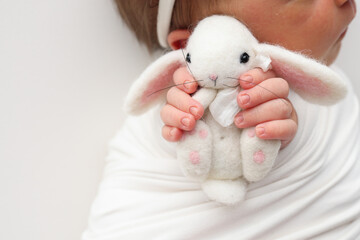 Sleep of a newborn in the first days of life. Portrait of a newborn one week old baby with a cute soft toy plush rabbit on a white background. Cute little fingers and hands of a child.