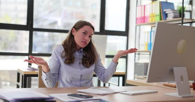 Unsure woman working at computer sits at workplace and shrugs