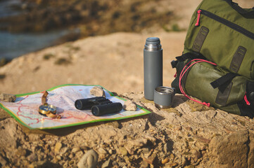 Still life backpack and thermos flask on the cliff against Atlantic ocean background while waves...