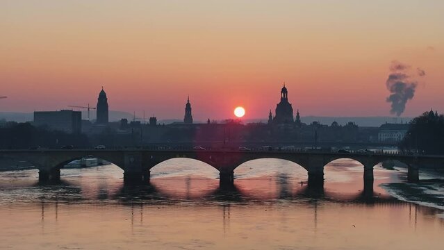 Total Aerial view over the Dresden Elbe at sunset in the winter with sun backlit. Drone move backwards. Cars driving over the bridge with a church in the background