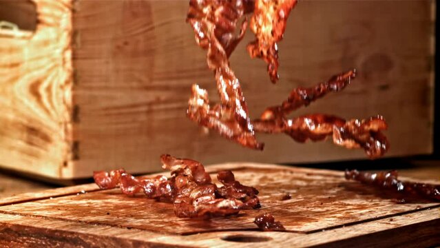 Roasted slices of bacon fall on a wooden table. Filmed on a high-speed camera at 1000 fps. High quality FullHD footage