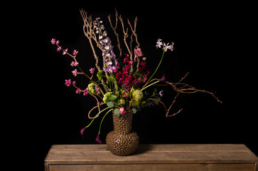 rainbow flower arrangement with colored silk flowers in vase. Black background. Studio photo.