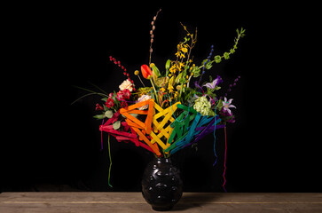 rainbow flower arrangement with colored silk flowers in vase. Black background. Studio photo.