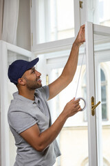 Fototapeta na wymiar Young man putting sealing tape on window in house.