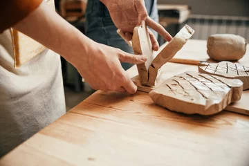 Deurstickers A potter cuts a large piece of raw clay into pieces with a string. Preparing for clay modeling in the workshop, close-up © Irina