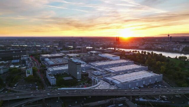 Aerial flight with sun backlit over the city of cologne with sunset and colorful sky. There is evening traffic on Highway. Drone moves around the fair.