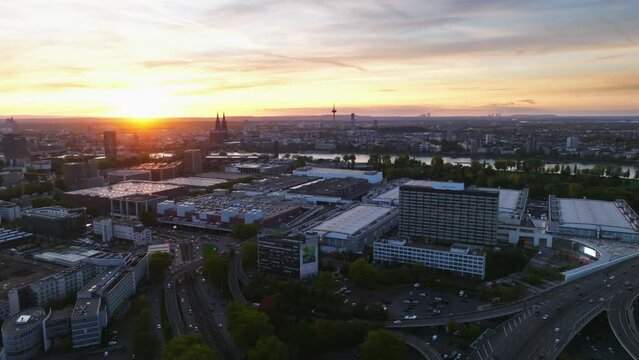 Aerial flight with sun backlit over the city of cologne with sunset and colorful sky. There is evening traffic on Highway. Drone move up backwards