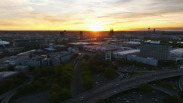 Aerial flight with sun backlit over the city of cologne with sunset and colorful sky. There is evening traffic on Highway. Drone move up.