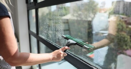 Closeup of hands cleaning windows with squeegee