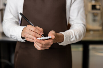 Obraz na płótnie Canvas Pizzeria worker in apron making notes for order preparation