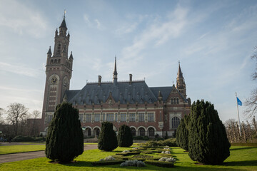 International Court of Justice The Hague, Netherlands on clear sunny day shot from street level. shot of clock tower main entrance with front garden and pruned trees