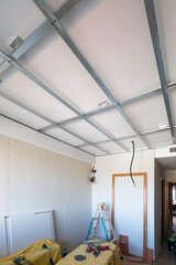Renovation of a home room with plasterboard insulation in the ceilings and half-constructed walls with the metal structure of the ceiling visible and construction material on the floor.