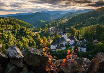 Village Spania Dolina. Fall in Slovakia. Old mining village. Historic church in Spania dolina. Autumn colored trees at sunset. - obrazy, fototapety, plakaty
