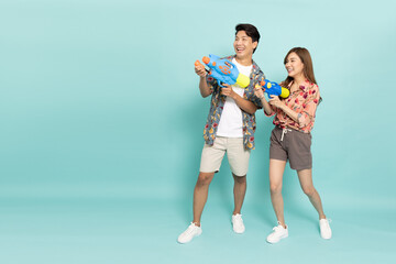 Young Asian couple in summer outfits holding water guns plastic for Songkran festival in Thailand isolated on green background - 723189971