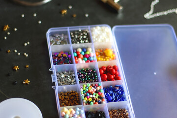 Box with colorful beads, string, wire, chain, scissors, pliers and hammer on dark background. Various jewelry making supplies. Selective focus.