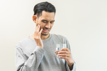 Portrait of male suffering sensitive teeth,tooth pain asian young man hand holding glass of cold...