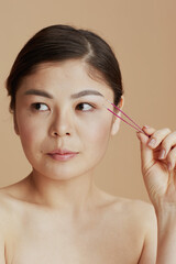 young asian woman with tweezers against beige background