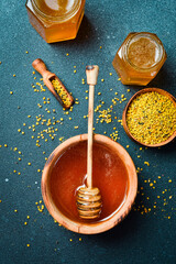 Organic honey in wooden bowl with honey stick and flower pollen. Honey background. Top view.