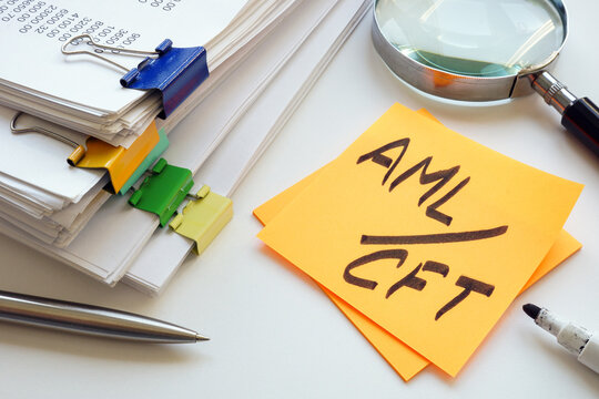 Stack of papers, magnifying glass and abbreviation AML CFT anti-money laundering and combating the financing of terrorism.