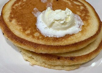 A side view of two pancakes on a plate with a large dollop of melting butter