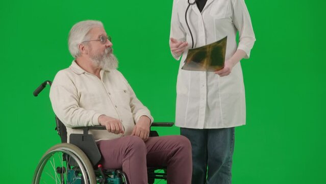 Portrait of aged disabled man on chroma key green screen. Senior man in wheelchair with doctor looking at lungs x-ray picture.
