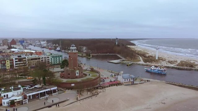 In a January winter drone film, a small cruise ship enters Kolobrzeg port. The footage showcases beach walkers, soaring seagulls, golden Baltic sands, Kolobrzeg lighthouse, and stormy waves.