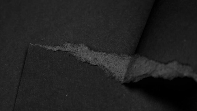 Tearing a black paper sheet with ragged edges. Torn dark grey layered material close up