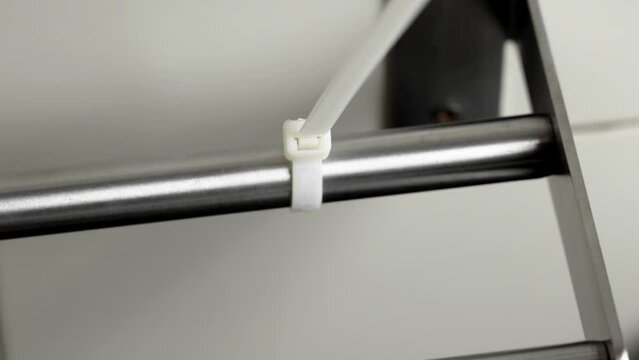 The process of tightening a plastic cable tie on a metal detail close up