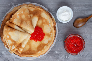 Stack of russian thin pancakes blini with red caviar and fresh sour cream