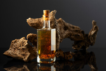 Bottle of spicy oil and olive tree snag on a black background.