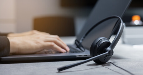 close up headset with employee man hand type work on keyboard laptop at desk for advise or share information to customer for hotline call center and service provider concept