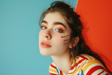 Portrait of a confident young woman looking at the camera with a funny expression and graphic eyeliner on her face. Self-assured woman having fun with a trendy makeup look in a studio.