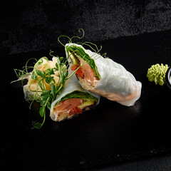 Salmon and avocado sprint roll with green pea sprouts on a black textured slate